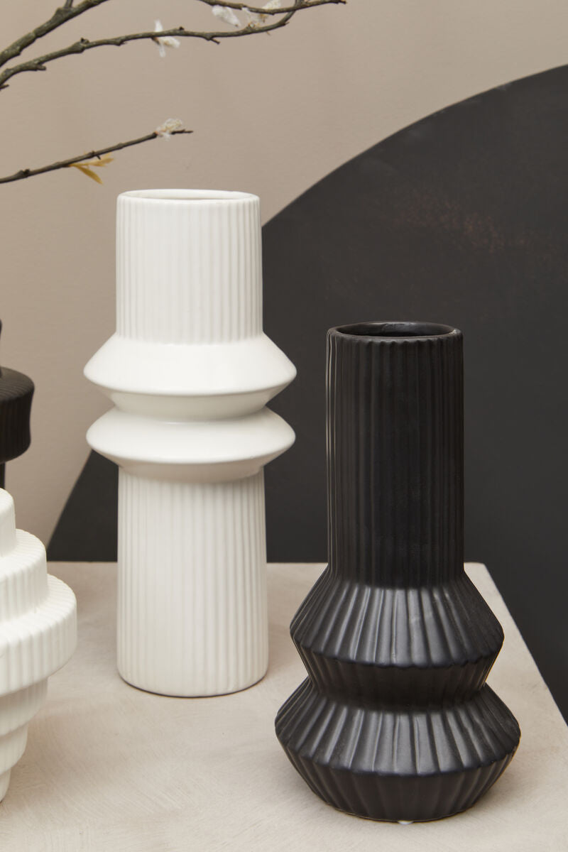 Three vases, two white and one black, on a surface with a neutral background.