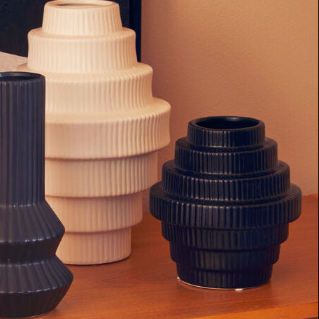 Set of black and white vases on a wooden surface with a abstract painting in the background.