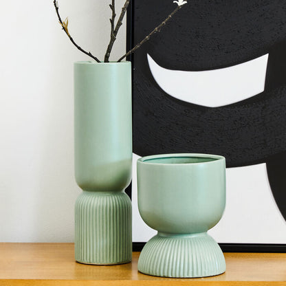 Two green vases on a wooden surface with a black and white abstract artwork in the background.