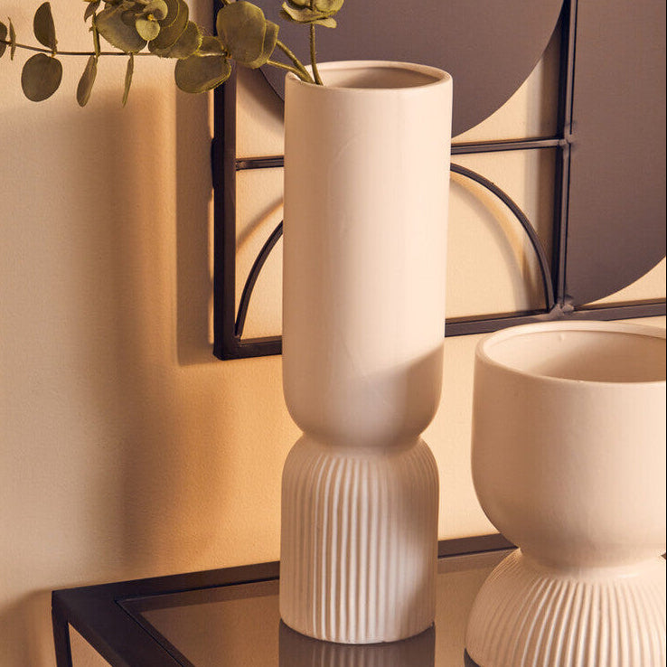 Two beige textured vases on a black glass table with a decorative wall mirror in the background.