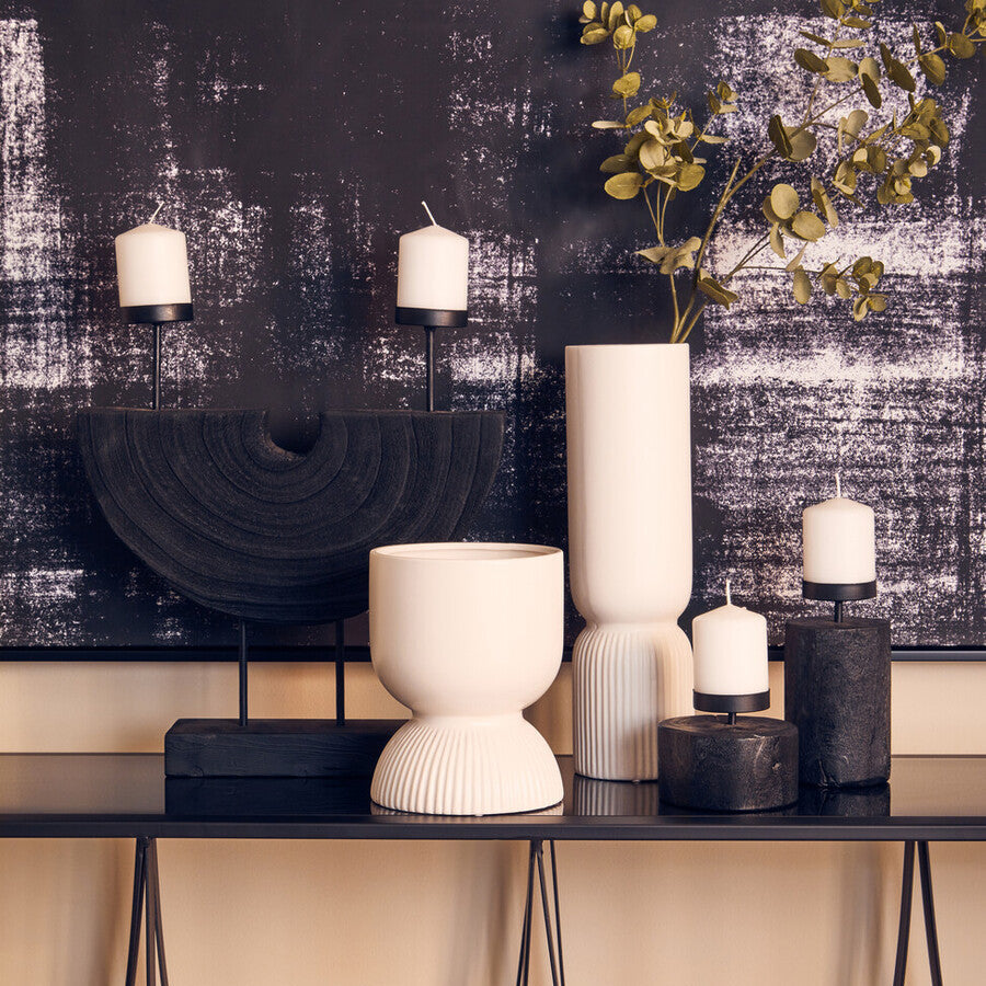 Decorative setting with vases, candles, and a plant against a textured wall.