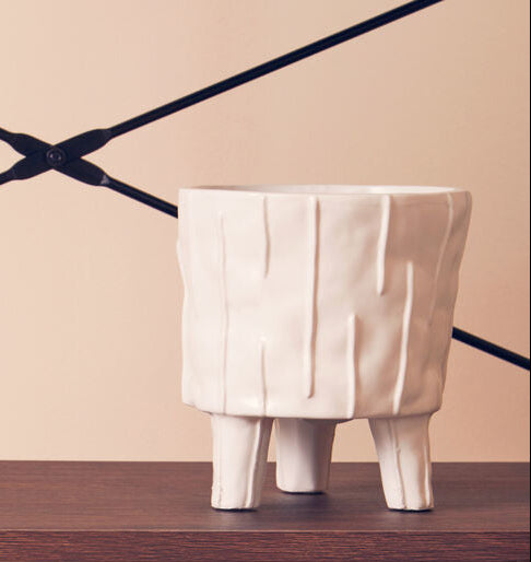 Two white geometric planters with plants on a wooden shelf against a beige wall.