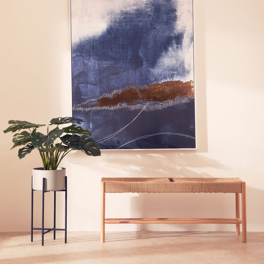 Abstract painting on a wall with a plant and bench in a room