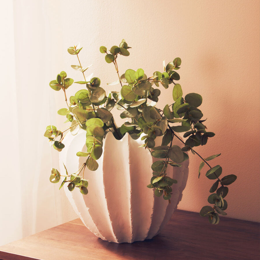 White vase with greenery on a wooden surface against a light background