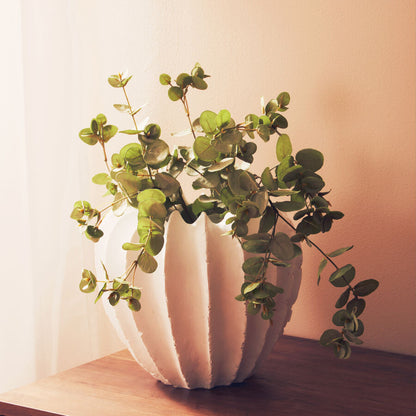 White vase with greenery on a wooden surface against a light background