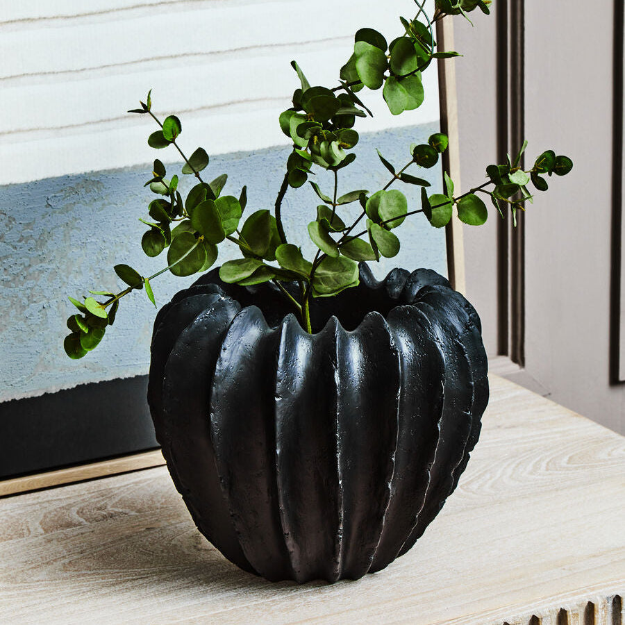 Black textured vase with green leaves on a wooden surface