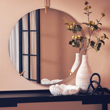 Round mirror on a wall with a vase and decorative items on a shelf below.