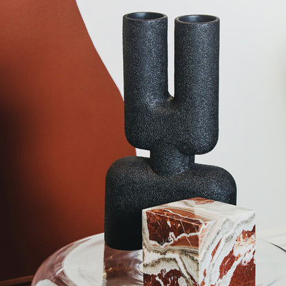 Decorative black vase with a marble cake on a reflective surface