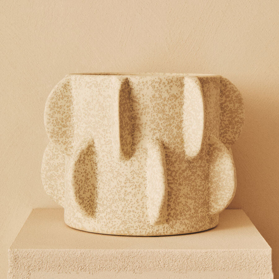 Textured ceramic vase on a beige pedestal against a beige wall