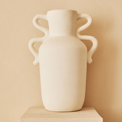 White vase with handles on a beige pedestal against a beige wall