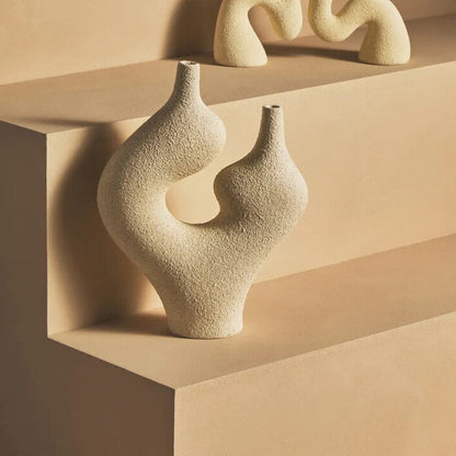 Ceramic candle holders and vases on a beige shelf with a dark background