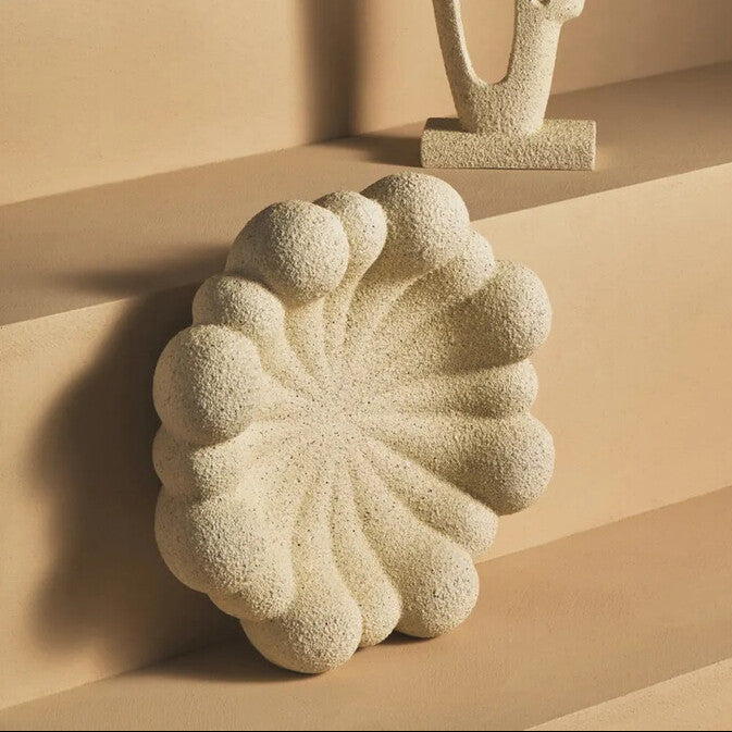 Two abstract stone sculptures on a beige platform with a dark background