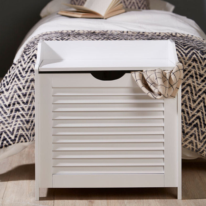 White storage bench with a patterned cushion and blanket in a bedroom setting.