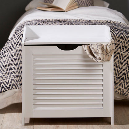 White storage bench with a patterned cushion and blanket in a bedroom setting.