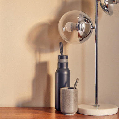 Desk lamp, water bottle, and cup on a wooden surface with a neutral background