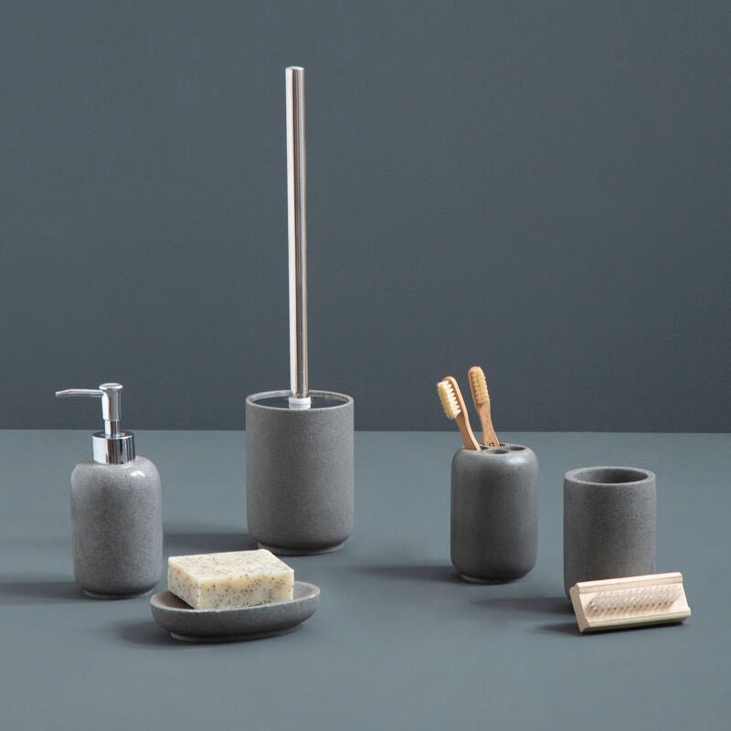 Set of gray bathroom accessories including a soap dispenser, brush holder, and cups on a dark surface with a dark background.