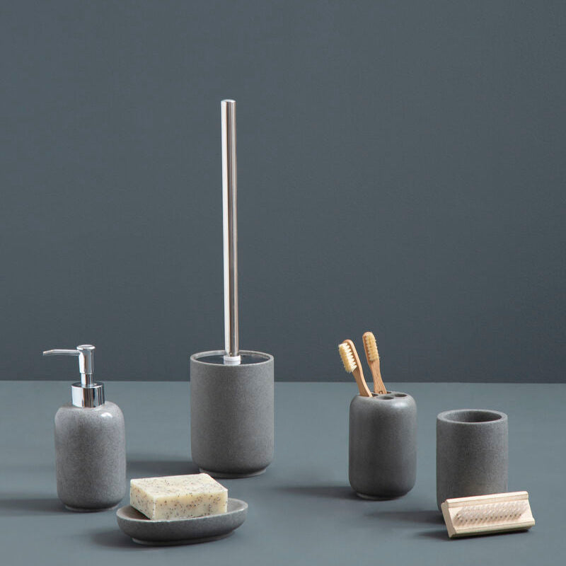 Set of gray bathroom accessories including a soap dispenser, brush holder, and cups on a dark surface with a dark background.