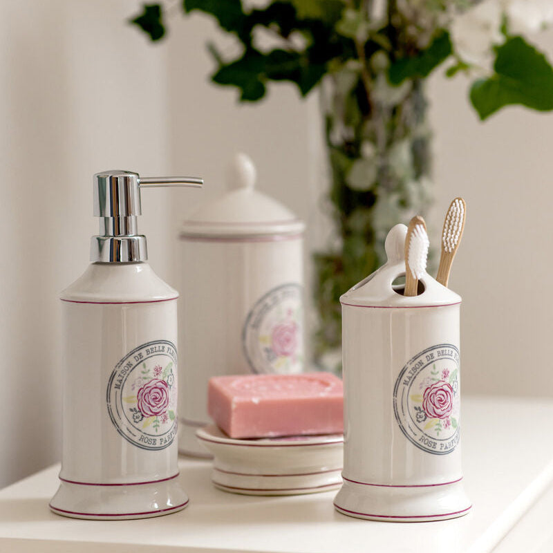 Bathroom accessories including a soap dispenser, canisters, and a bar of soap on a white surface with flowers in the background.