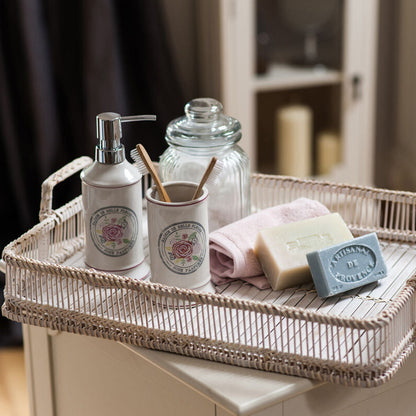 Bathroom tray with toiletries including a soap dispenser, jars, and a bar of soap on a wooden surface.