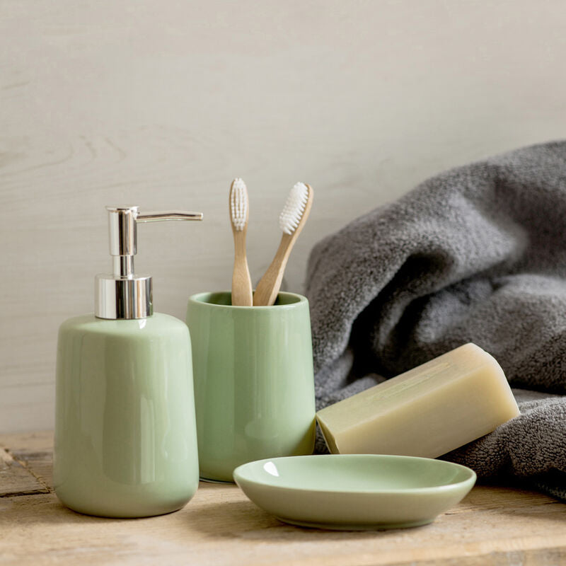 Bathroom set with green ceramic items including a soap dispenser, toothbrush holder, and soap on a wooden surface.