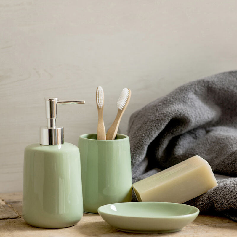 Bathroom set with green ceramic items including a soap dispenser, toothbrush holder, and soap on a wooden surface.
