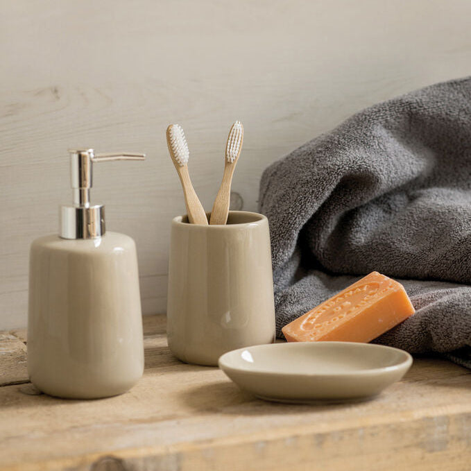 Bathroom counter with ceramic soap dispenser, toothbrush holder, and soap on a wooden surface.