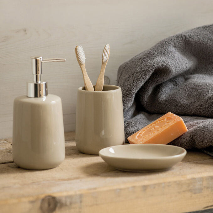Bathroom counter with ceramic soap dispenser, toothbrush holder, and soap on a wooden surface.