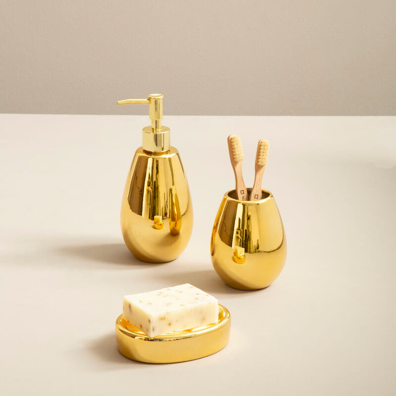Gold bathroom accessories including a soap dispenser, dish, and holder on a beige background