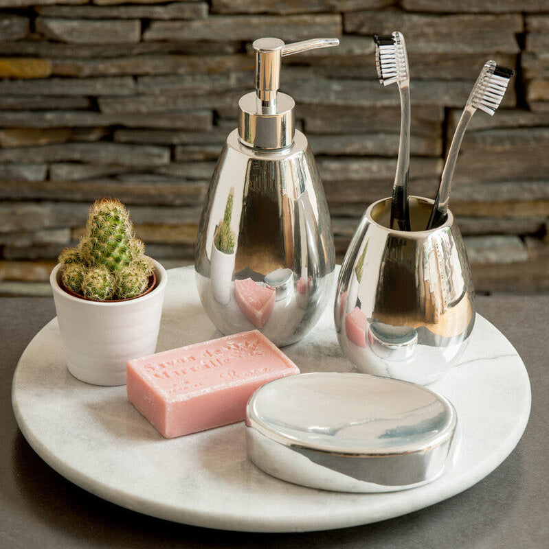 Bathroom counter with silver dispenser, toothbrush holder, soap, and cactus plant against a stone wall.