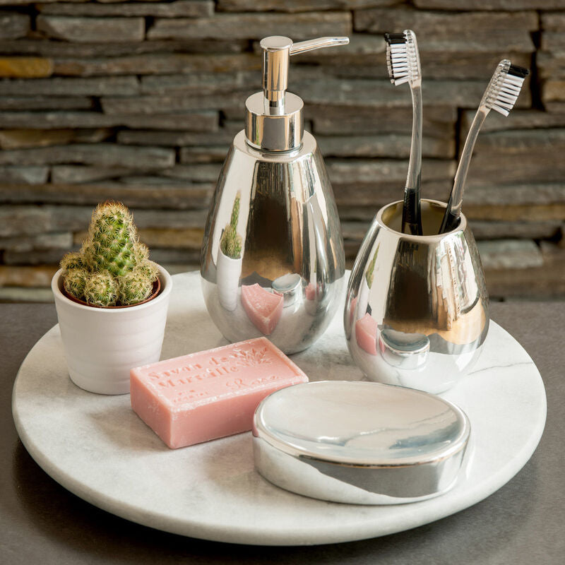 Bathroom counter with silver dispenser, toothbrush holder, soap, and cactus plant on a marble tray.