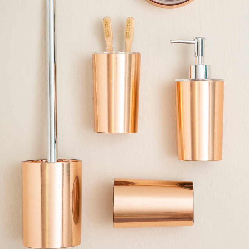 Set of gold bathroom accessories including a soap dish, cups, and dispenser on a beige wall.