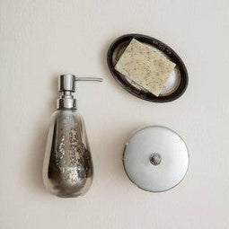 Decorative soap dispenser with a bar of soap on a small round tray against a light background