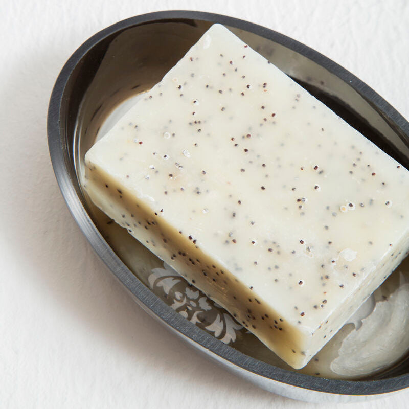 Bar of soap with specks on a metal soap dish against a white background
