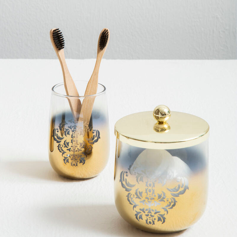 Two gold toothbrush holders with decorative lids on a white surface.