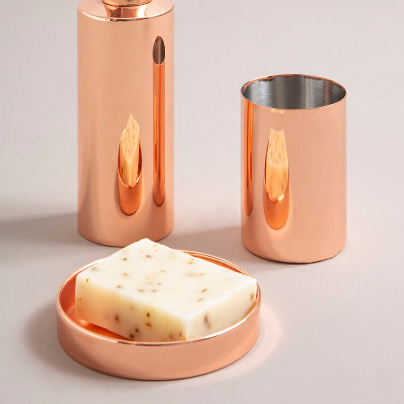Copper bathroom accessory set with soap dish, dispenser, and cup on a light gray background