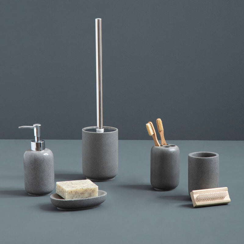 Set of gray bathroom accessories including a soap dispenser, brush holder, and cups on a dark surface with a dark background.