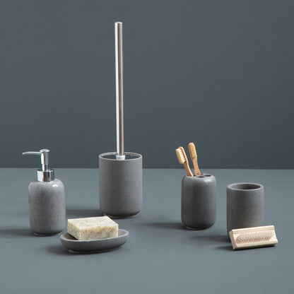 Set of gray bathroom accessories including a soap dispenser, brush holder, and cups on a dark surface with a dark background.
