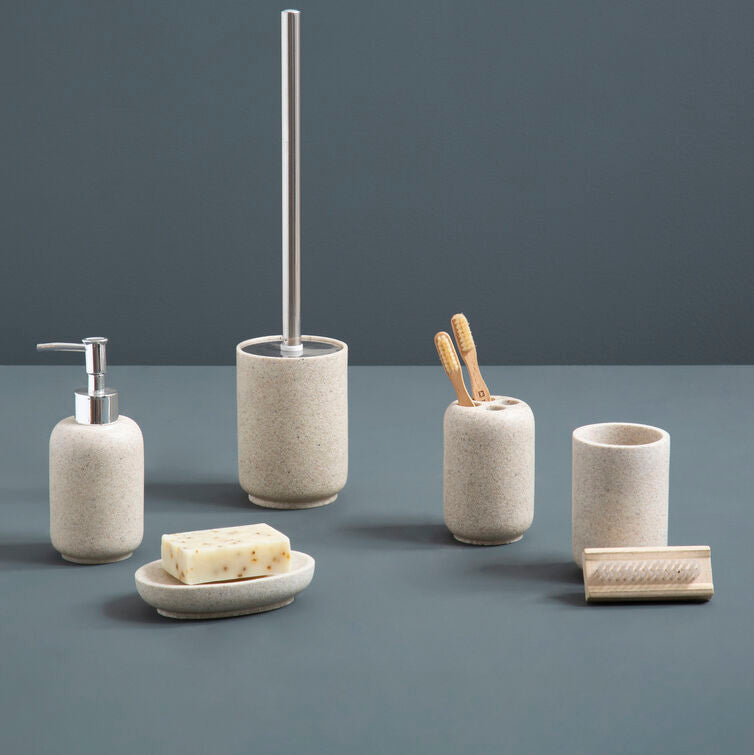 Set of bathroom accessories including a soap dispenser, brush holder, and cup on a gray surface with a dark gray background.
