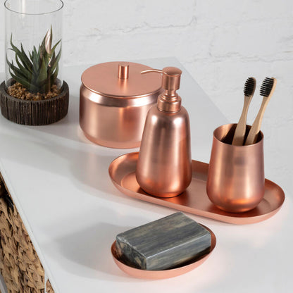 Copper bathroom accessories including a soap dish, bottle, and cup on a white surface with a plant in the background.