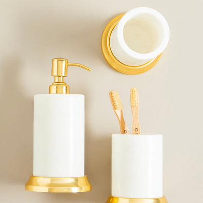 Bathroom accessories set with gold fixtures and white containers on a beige wall.