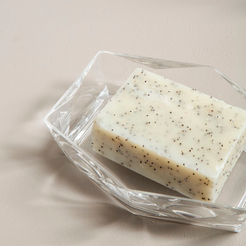 Bar of soap with specks on a clear dish against a neutral background