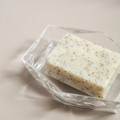 Bar of soap with specks on a clear dish against a neutral background