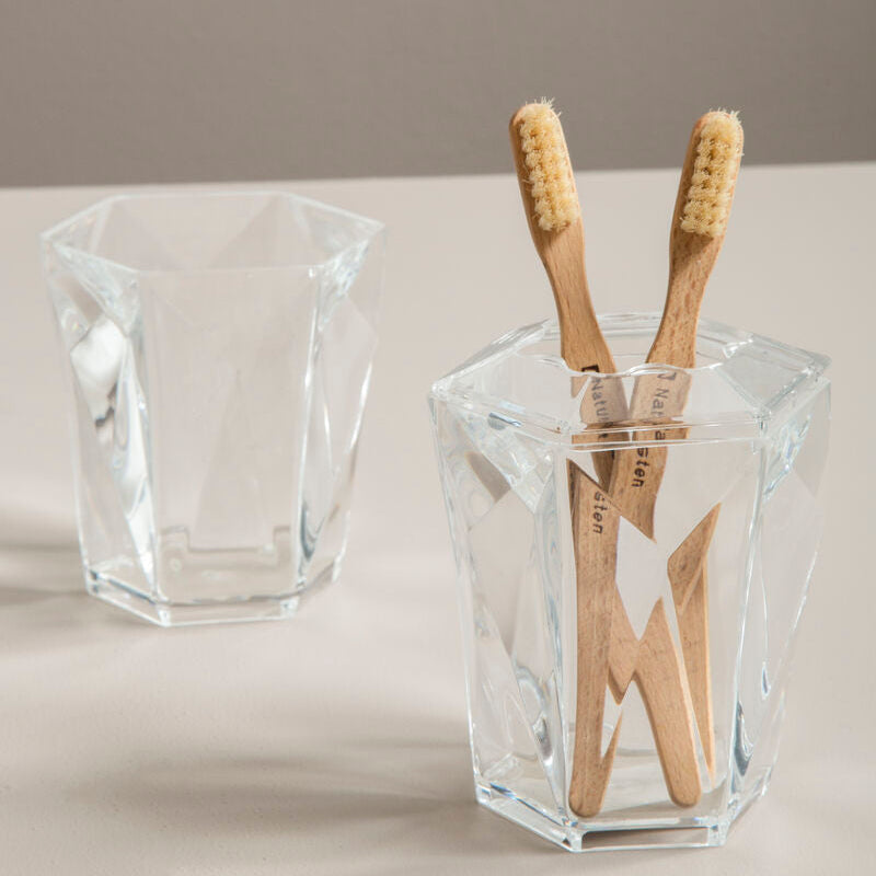 Clear glass holder with wooden toothbrushes on a neutral background
