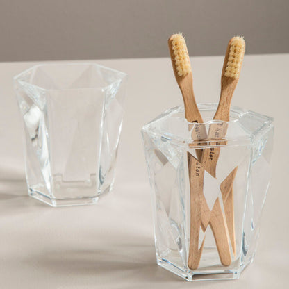 Clear glass holder with wooden toothbrushes on a neutral background