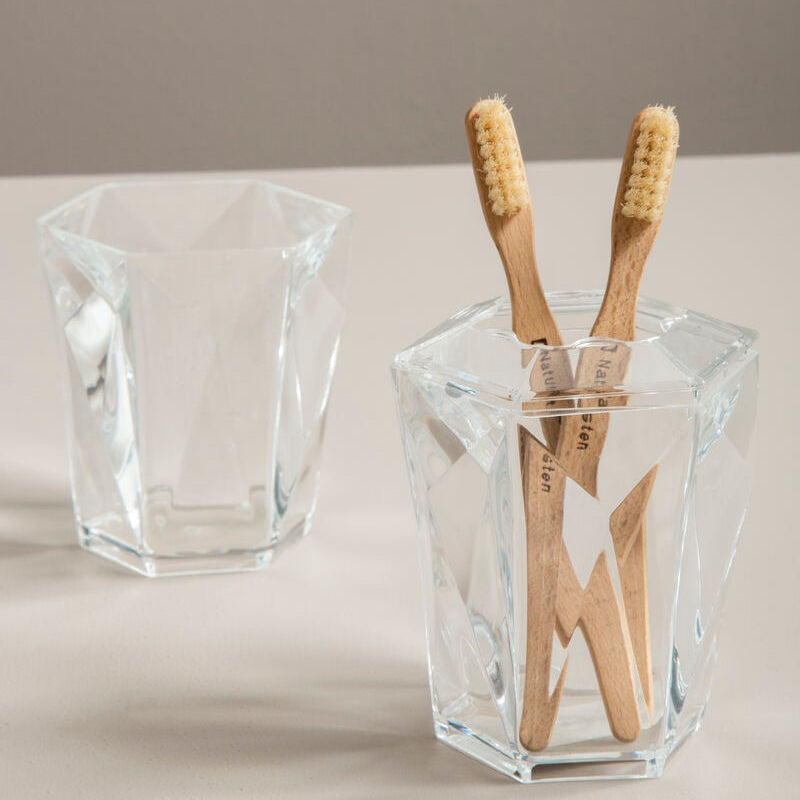 Clear glass holder with wooden toothbrushes on a neutral background