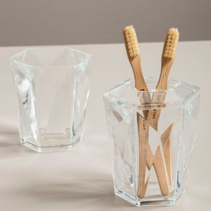 Clear glass holder with wooden toothbrushes on a neutral background
