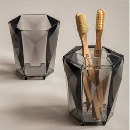 Two geometric glass containers with bamboo toothbrushes on a neutral background