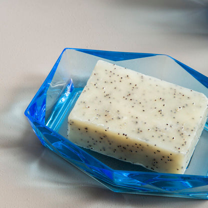 Bar of soap with specks on a blue soap dish on a light surface