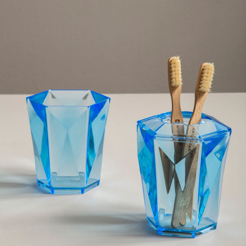 Two blue geometric glass holders with toothbrushes on a neutral background