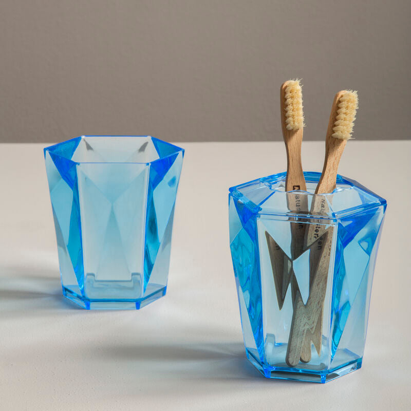 Two blue geometric glass holders with toothbrushes on a neutral background